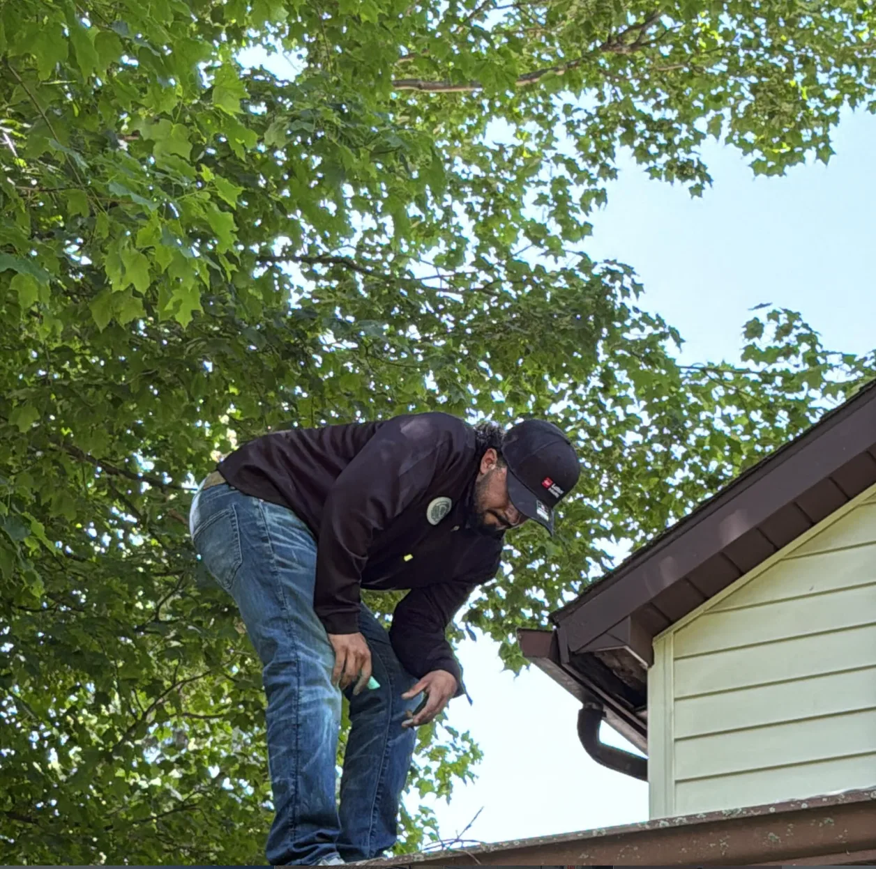Lake Acer Roofing crew member standing on a roof under green maple trees, checking the edge of the roofline above the gutter