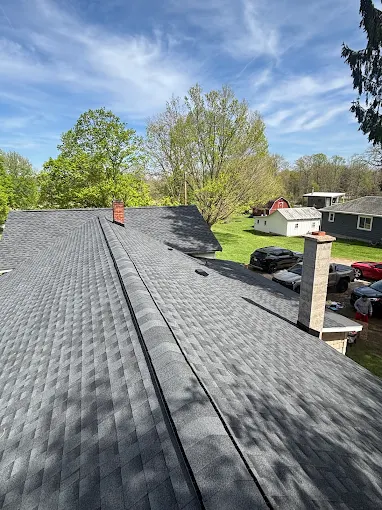 Newly shingled charcoal roof running toward a brick chimney, with a neighboring red barn and open lawn below